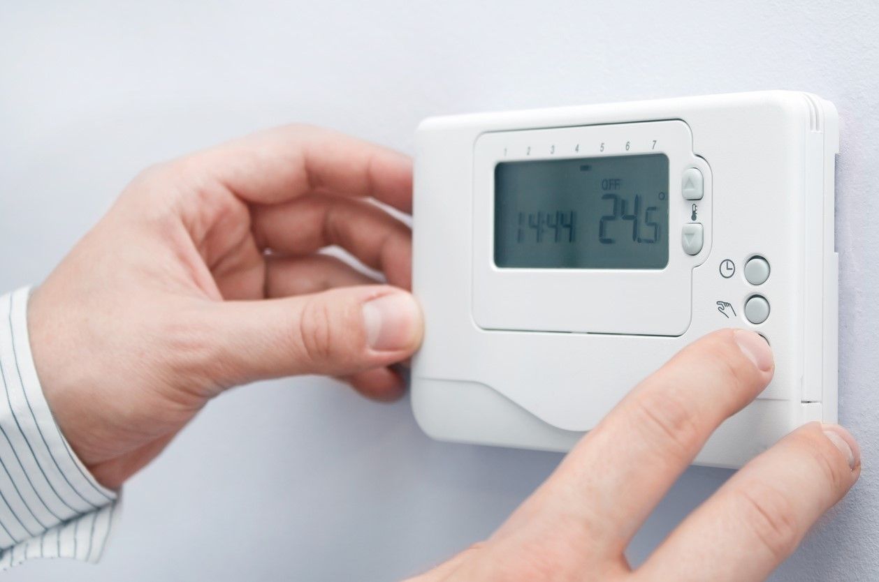 Modern white thermostat on a while wall. Set of hands pressing buttons on the right side.